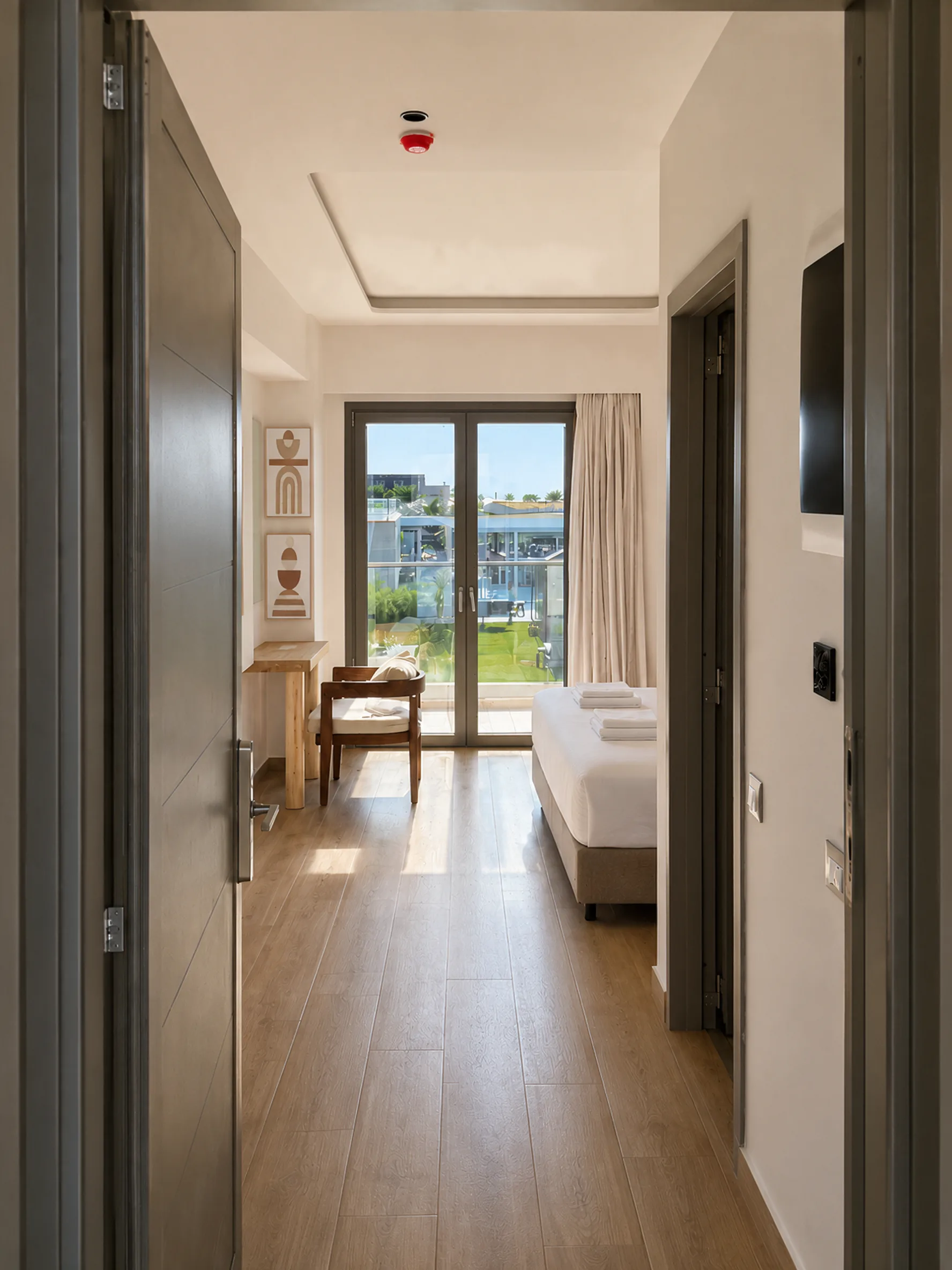The room seen from the entrance hall, wooden floor leading past the bed to the balcony doors and the garden